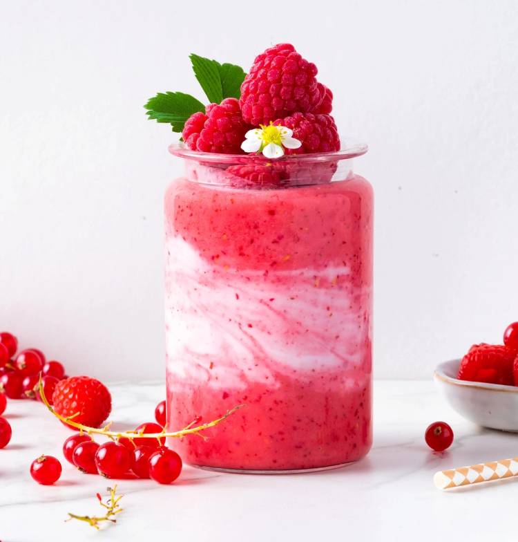 Bringebær- og ripssmoothie i et glass med friske bær og mynte på toppen