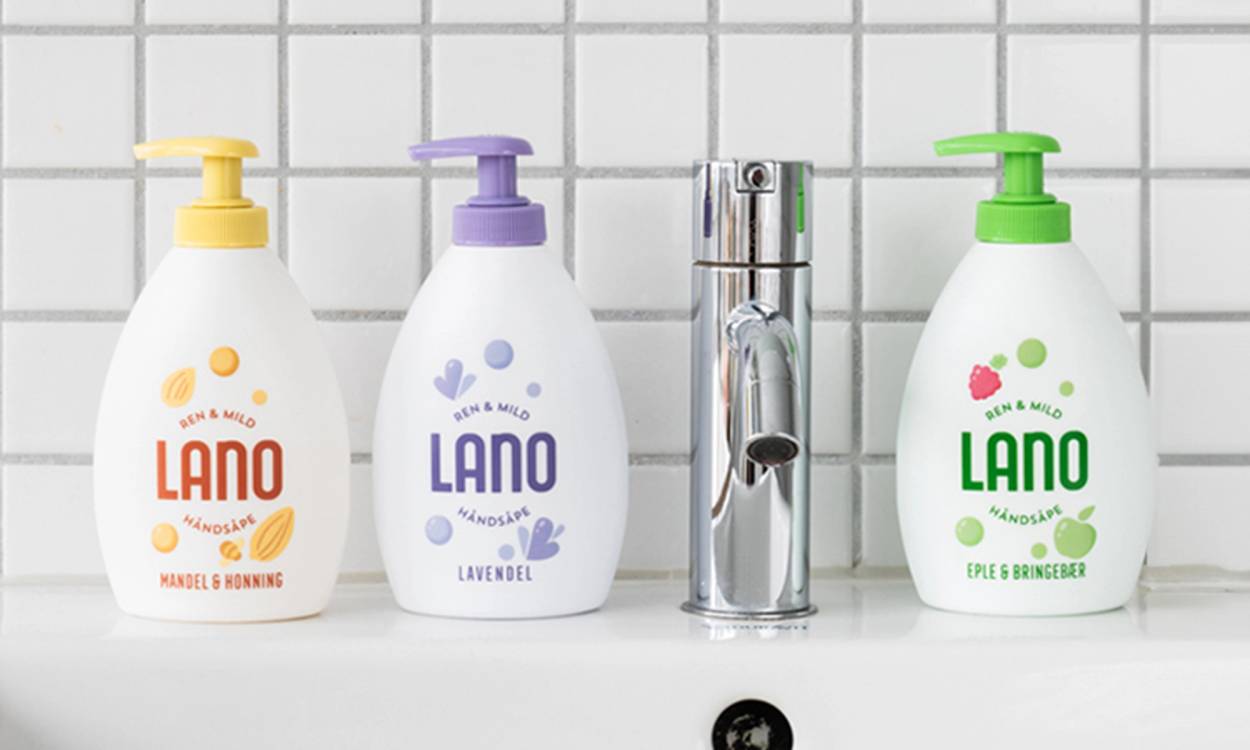 Tre flasker med duftsåpe i ulike farger står på en kjøkkenbenk foran en kjøkkenkran.