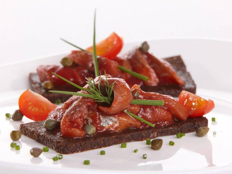 Sildakongen med sild, grønne urter, kapers og en mørk kjeks på en hvit tallerken