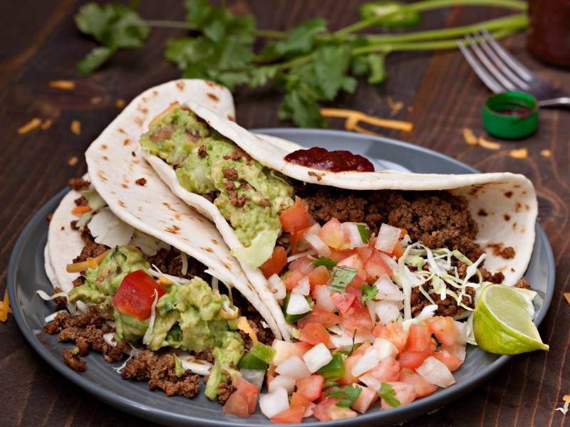 Klassisk norsk taco med kjøttdeig, guacamole, salsa, rømme og lime på en tallerken.