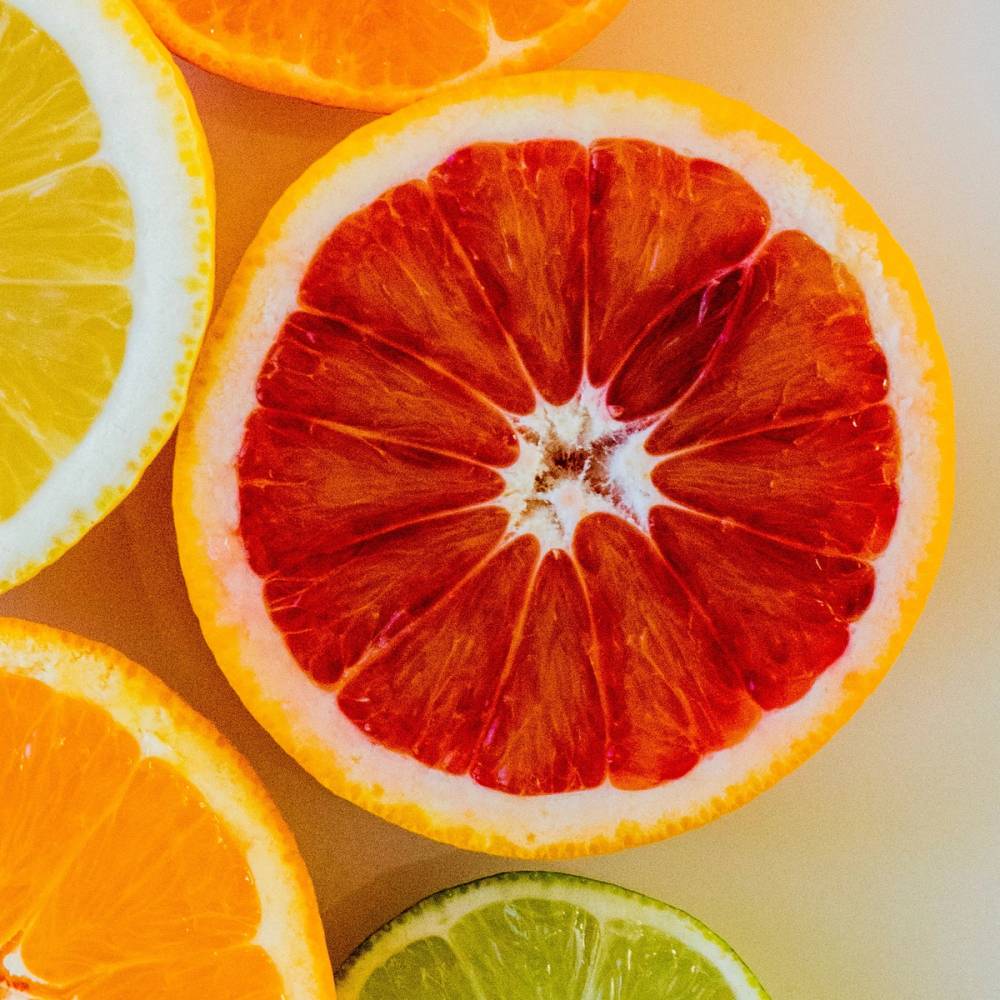 Skarne sitrusfrukter, inkludert en blodappelsin, en sitron og en lime, på et lyst underlag.