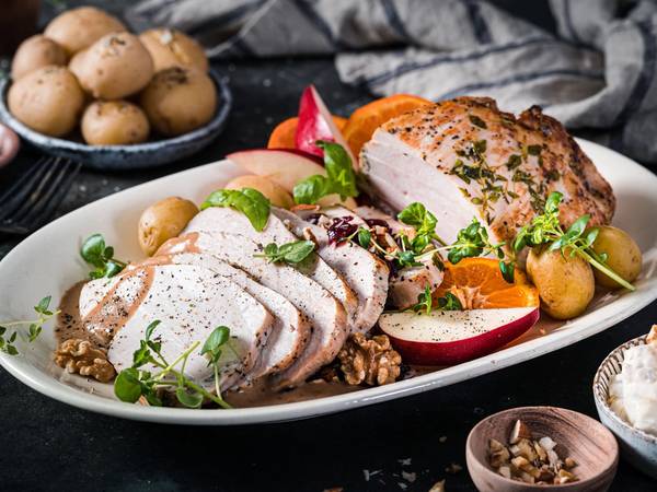 Kalkunbryst med grønnsaker og poteter på en hvit tallerken, omgitt av små boller med saus og krydder, på et mørkt bord.