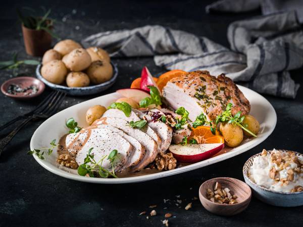 Kalkunbryst med grønnsaker og poteter på en hvit tallerken, omgitt av små boller med saus og krydder, på et mørkt bord.