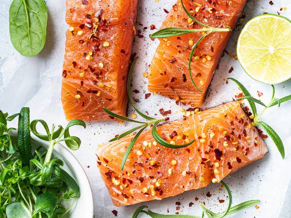 Tre laksefileter med sitronskiver og urter på en hvit bakgrunn, pyntet med pepper og grønne urter.