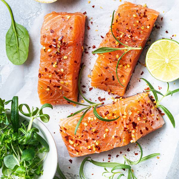 Tre laksefileter med sitronskiver og urter på en hvit bakgrunn, pyntet med pepper og grønne urter.