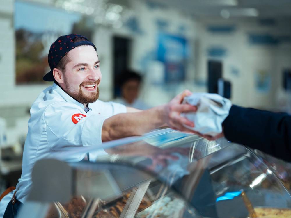 MENY-ansatt i ferskvaredisken rekker en vare til kunde.