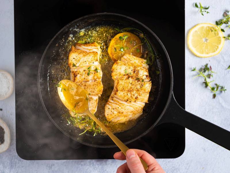 Steket torskefilet i en panne med sitronbiter og urter, sett fra oven.