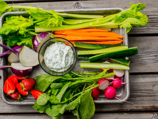 Et utvalg av friske grønnsaker som gulrøtter, reddiker, agurk, tomater, og ulike bladgrønnsaker på et trebrett.