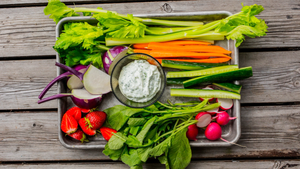 Et utvalg av friske grønnsaker som gulrøtter, reddiker, agurk, tomater, og ulike bladgrønnsaker på et trebrett.