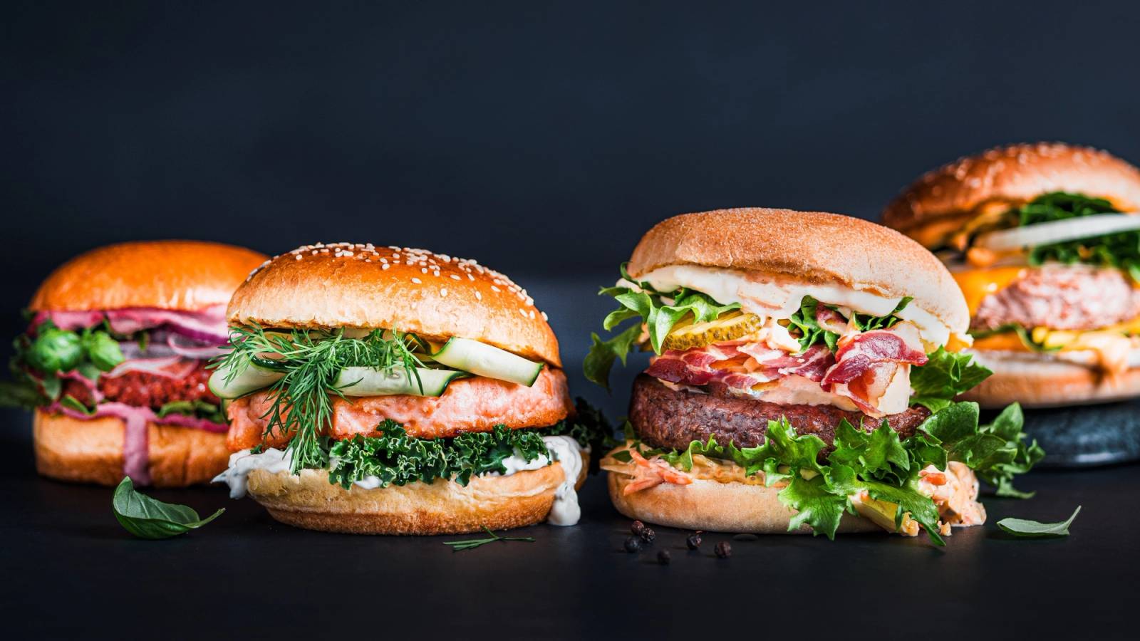 Fire burgere med ulike pålegg på en svart bakgrunn.