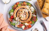 Salsiccia salat med mozzarella og parmaskinke på en tallerken med cherrytomater og grønt, omgitt av brød og bestikk.