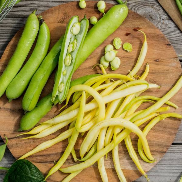 Ferske grønne bønner og gule bønner på et rundt trebrett, med noen bønner som er delt i to.