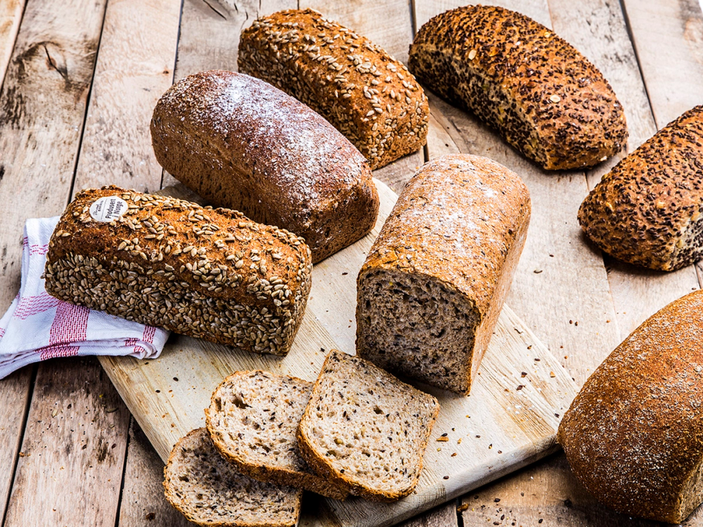 Ulike typer brød på et skjærebrett, med noen skiver av et av brødene foran.