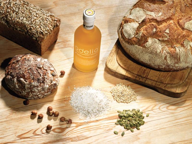Et brød, en flaske med Odelia-sirup, og ulike korn og frø på et trebord.