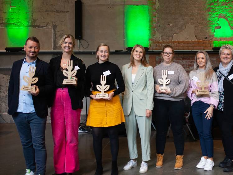 Personer som holder opp plantepriser under en seremoni i et rom med grønne lys på veggene.