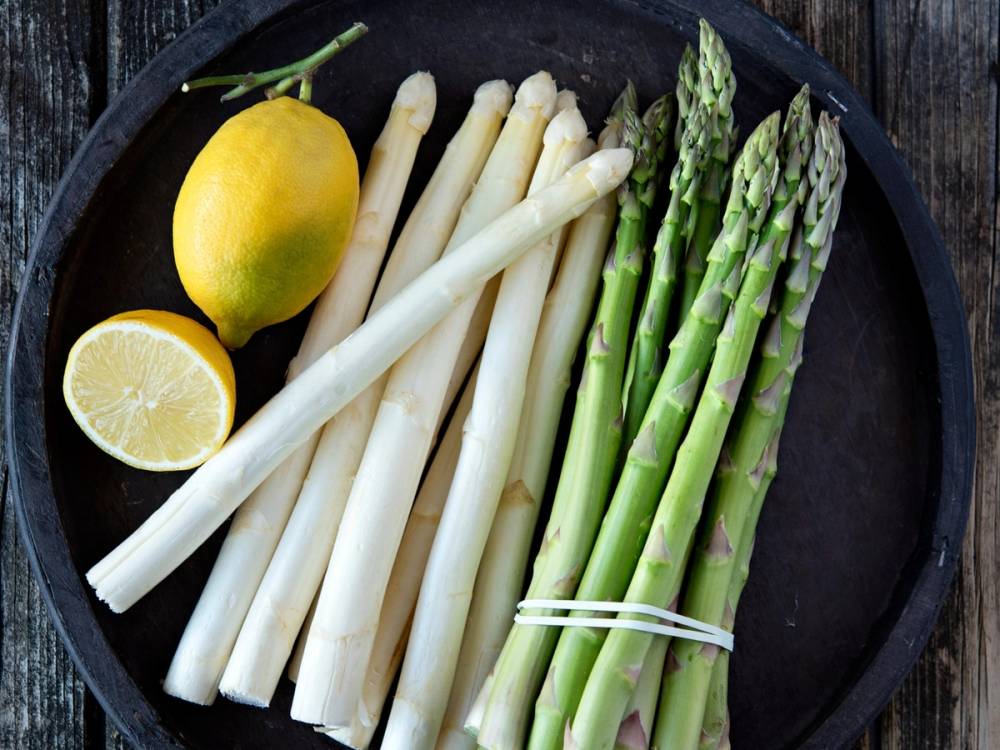 Ferske hvite og grønne asparges med sitron på en svart tallerken