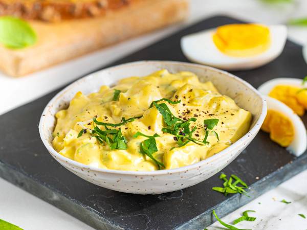Eggesalat i en hvit skål med hakket grønt på toppen, ser ut som en kremet blanding av egg og majones.