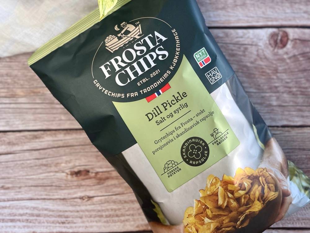 Pakkedeksel for Frosta Chips dillpickles med bilde av chips og dill, plassert på en treflate.