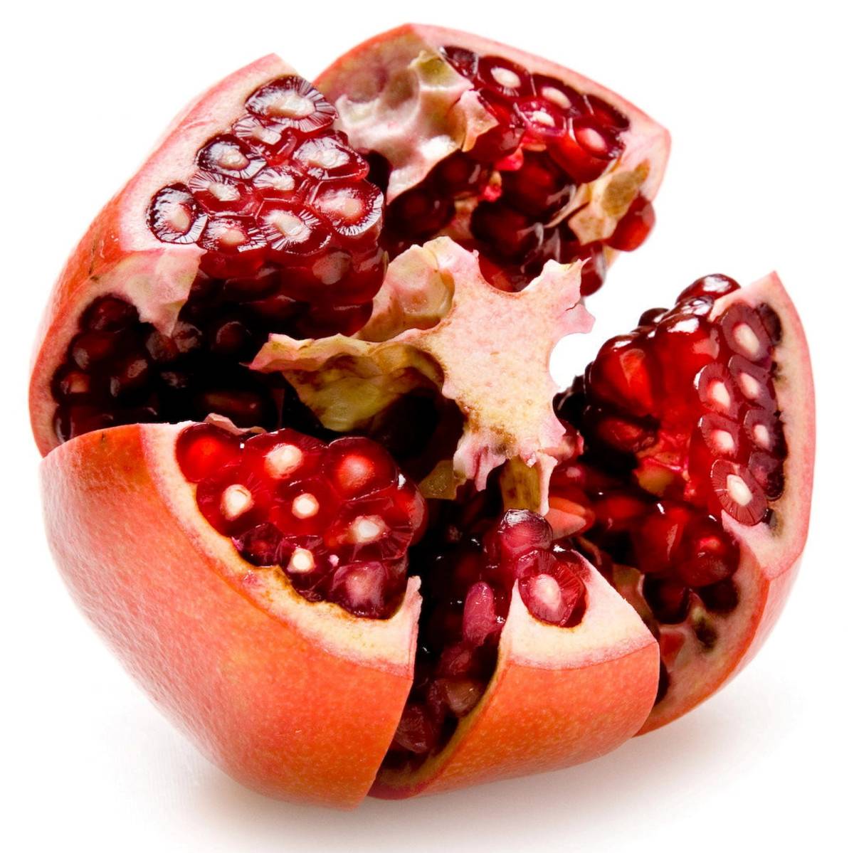 En delvis delt granateple med røde frø og hvite innvendige deler, mot en hvit bakgrunn.