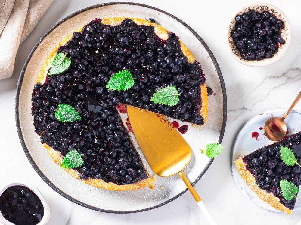 Blåbærpai med et stykke tatt ut og plassert på en tallerken, pyntet med mynteblader.