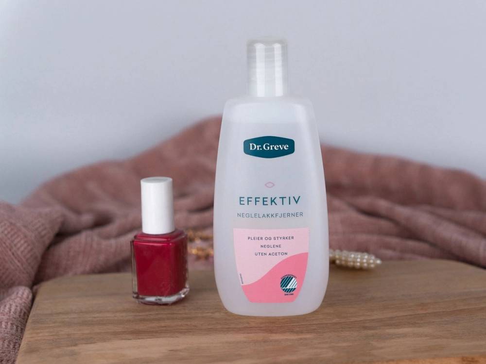 En flaske med neglelakkfjerner og en liten rød neglelakk på et bord med en rosa og beige bakgrunn.