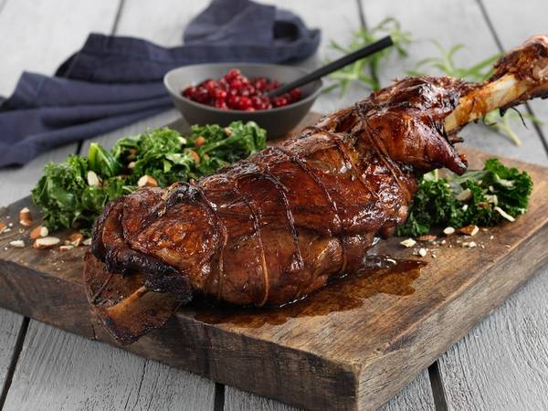 Stekt kje med urter og krydder, servert på et trebrett med grønnsaker og en liten skål med røde bær, på et lyst bord.