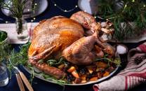 Stekt kalkun med grønnsaker og urter på et festbord, dekorert med granbar og lys.