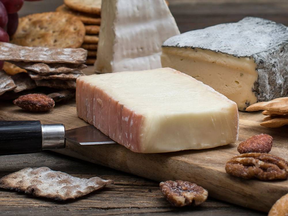 Taleggioost på et skjærebrett med kjeks og et stykke ost i bakgrunnen.