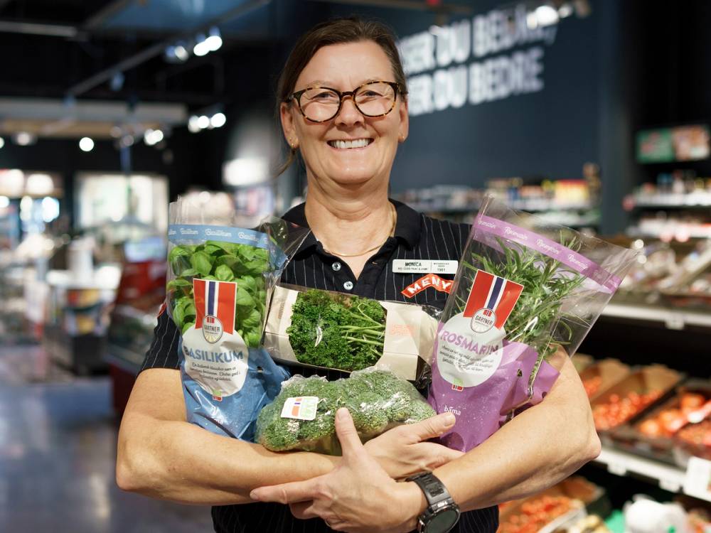 En person holder to poser med grønnsaker i en matbutikk, med hyller og lys i bakgrunnen.