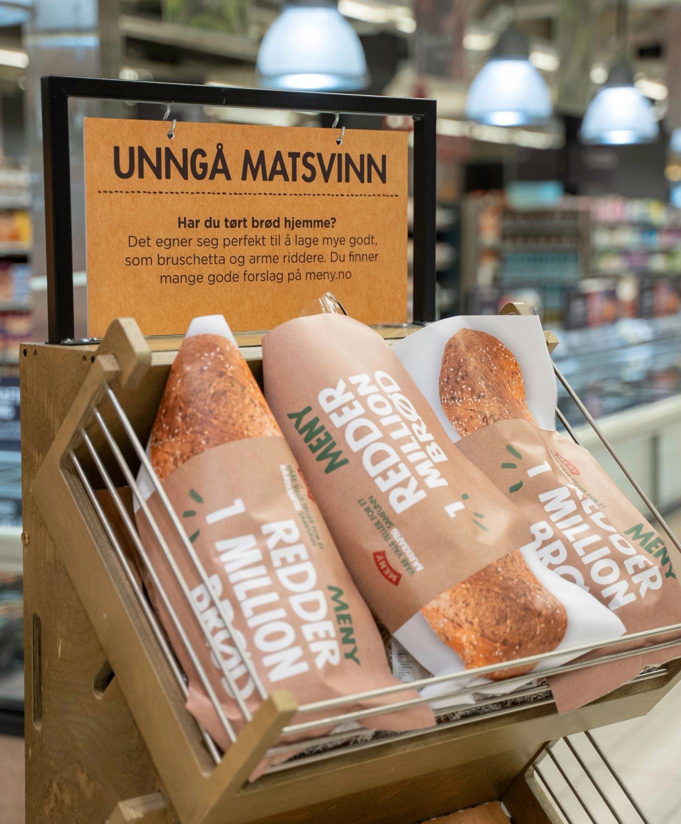 Pakker med ferdigmat i en butikkhylle med et skilt som advarer mot matsvinn, i en dagligvarebutikk.