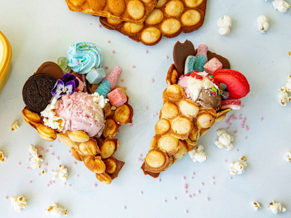 To iskremklynger med ulike godbiter og kjeks, pyntet med små marshmallows og fargerikt strøssel, på en lys bakgrunn.