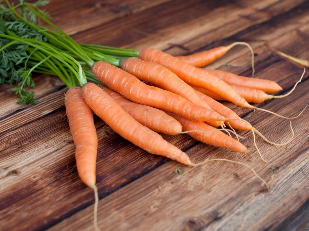 Ferske gulrøtter med grønne blader ligger på et trebord.