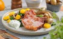 En tallerken med grillet kotelett, små poteter, en salat med mango og en klatt med hvit saus, omgitt av små skåler med tilbehør.