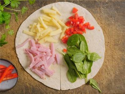 En tortilla wrap med skinke, ost, tomater, spinat og paprika på en treplate.