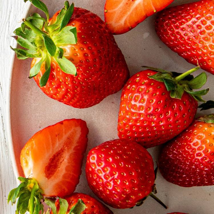 Ferske jordbær med grønne blader på en tallerken, noen er hele og noen er delt i to.