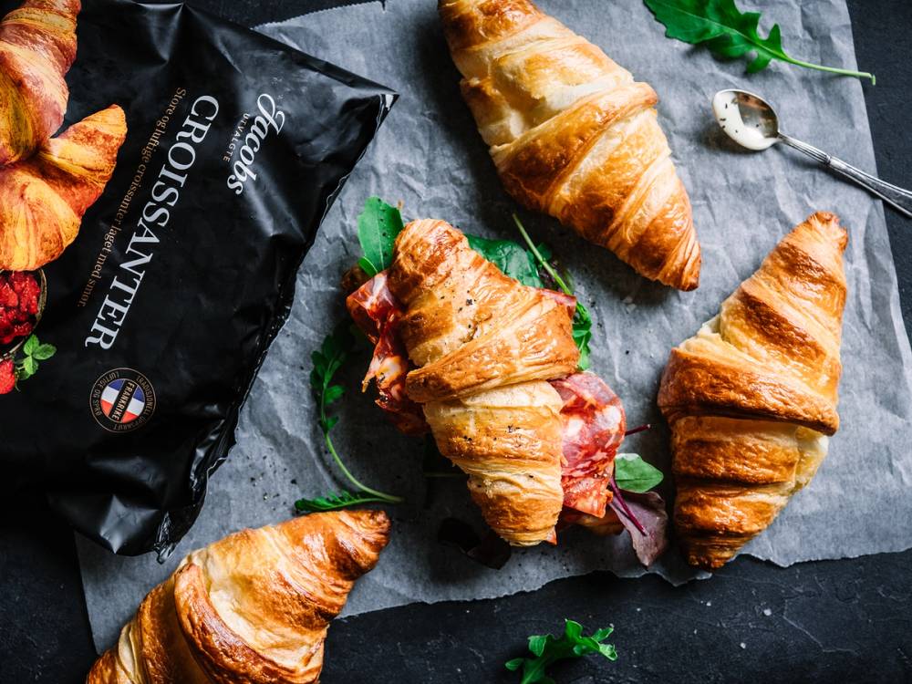 Ferske croissanter på et mørkt underlag med noen grønne blader og en pakke som heter Jacobs Croissanter