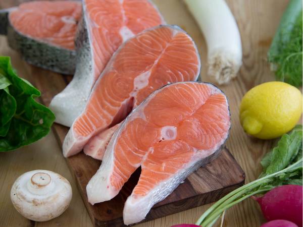 Skiver av fersk laks på et skjærebrett med grønnsaker og sitron rundt.