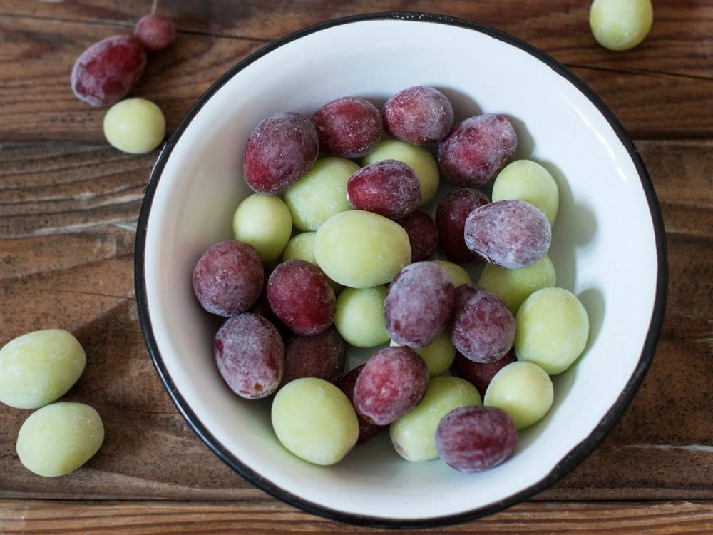 Frosne druer i en hvit skål på et trebord