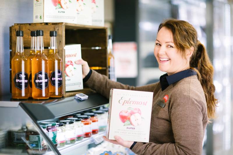 En kvinne ser på en meny i en butikkhyller med ulike produkter, med en bløt fokusert bakgrunn.