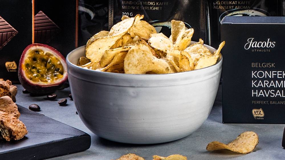 En stor hvit bolle fylt med potetgull på et bord med ulike snacks og en pakke med Jacobs chips i bakgrunnen.