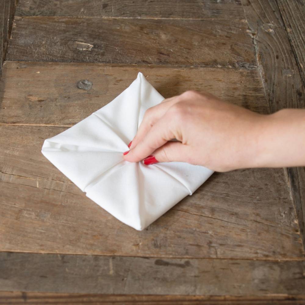 En person folder en hvit serviett til en juledekorasjon på et trebord.
