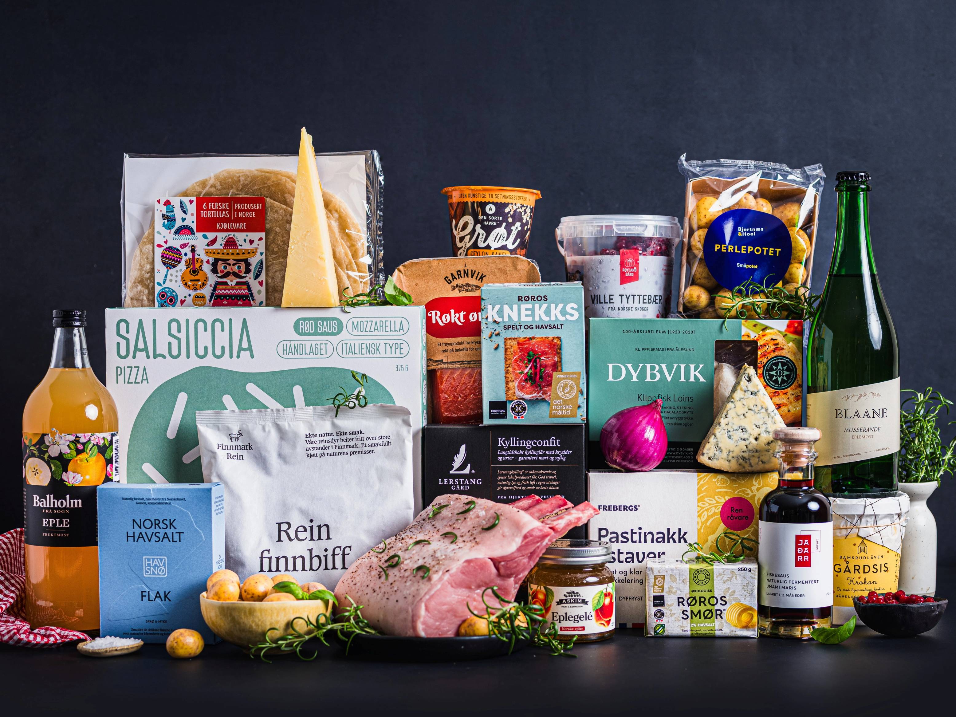 Et utvalg av matvarer og påskepynt på et bord, inkludert ost, kjøtt, sjokolade og en flaske vin, med påskepynt som en lilla egg og en liten påskekylling.