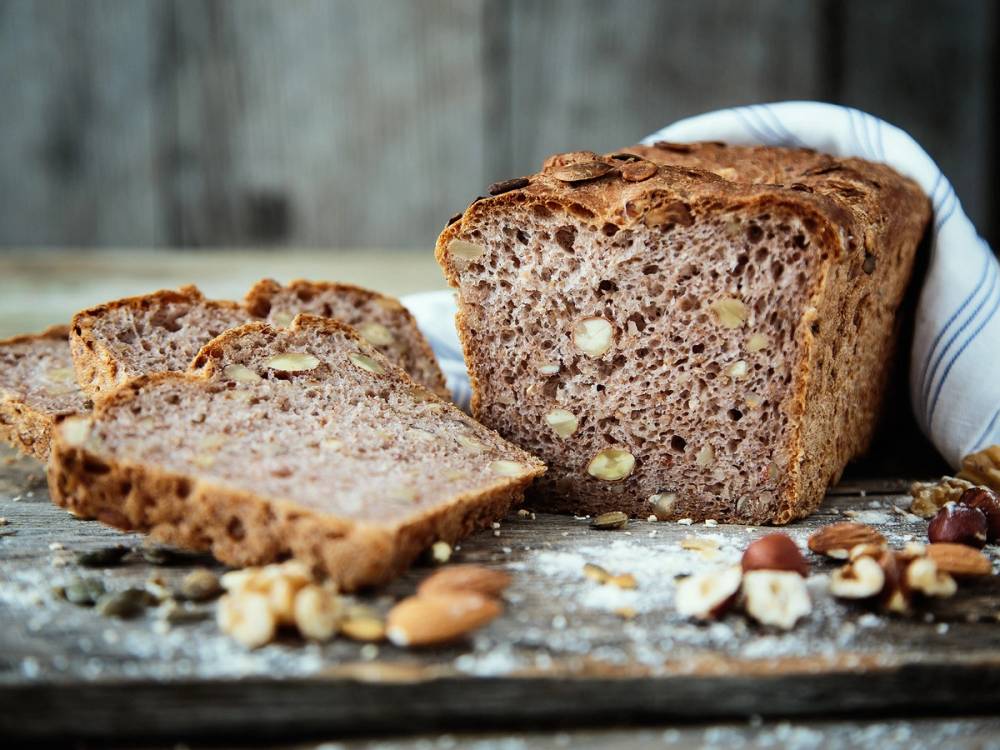 Grovbrød med nøtter som er delt i to, med noen nøtter og korn spredt rundt på bordet.