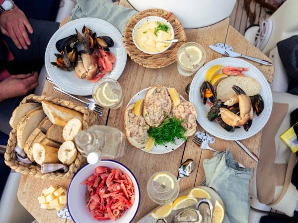 Et bord dekket med ulike retter, inkludert skalldyr, brød, ost og salat, sett fra oven.