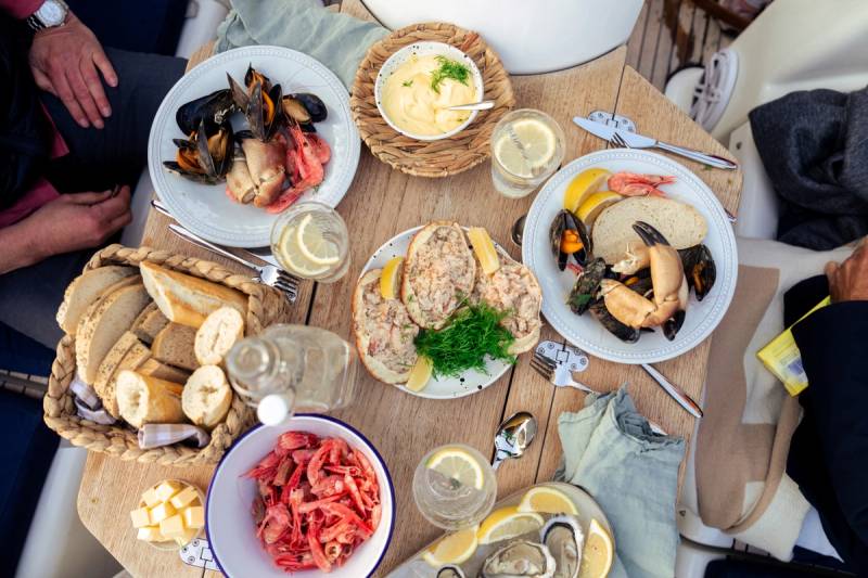 Et bord dekket med ulike retter, inkludert skalldyr, brød, ost og salat, sett fra oven.