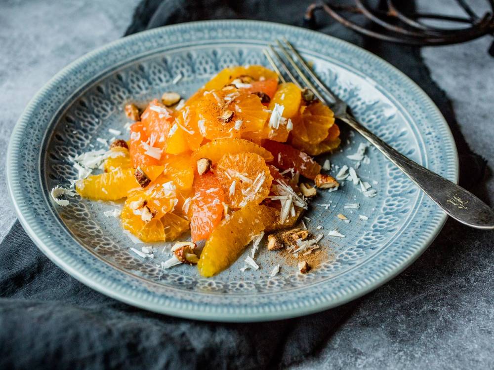 Sitrussalat med skiver av appelsin og sitron, toppet med kokosflak, servert på en blå tallerken.