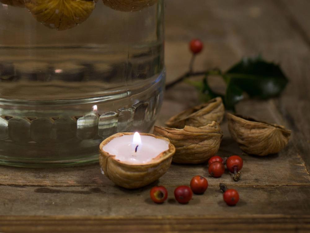 En valnøttskall med et tent lys inni, omgitt av små røde bær på et treverk.