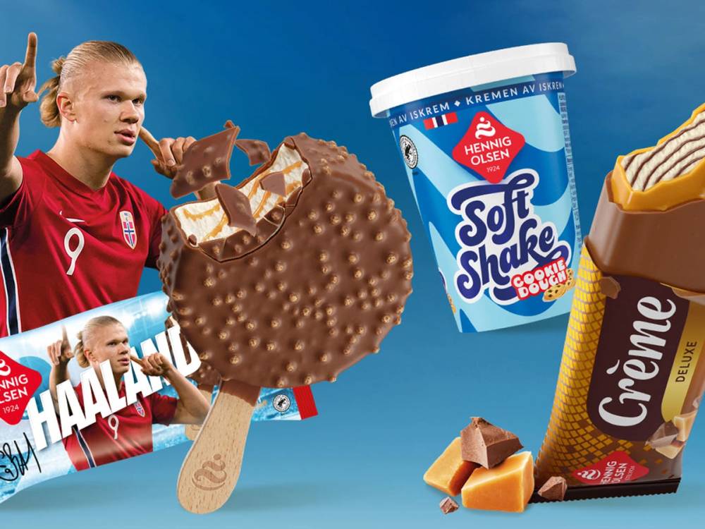 Hennig Olsen Soft Shake iskrem og sjokolade med en person i en rød fotballdrakt i bakgrunnen, mot en blå himmel.