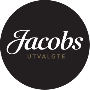 En svart rund logo med teksten 'Jacobs' i hvit kursiv og 'UTVALGTE' under i gullfarget skrift.