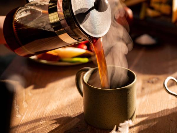 Kaffe helles opp i en kopp fra en stempelkanne, med damp som stiger opp.